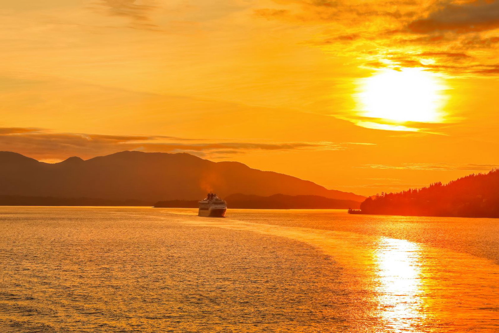 The sun sets over a cruise ship casting yellow light over the water