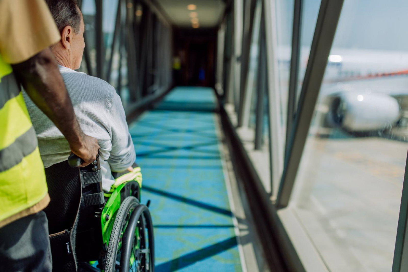 A air traveller being pushed down an air bridge onto an aircraft in a wheelchair