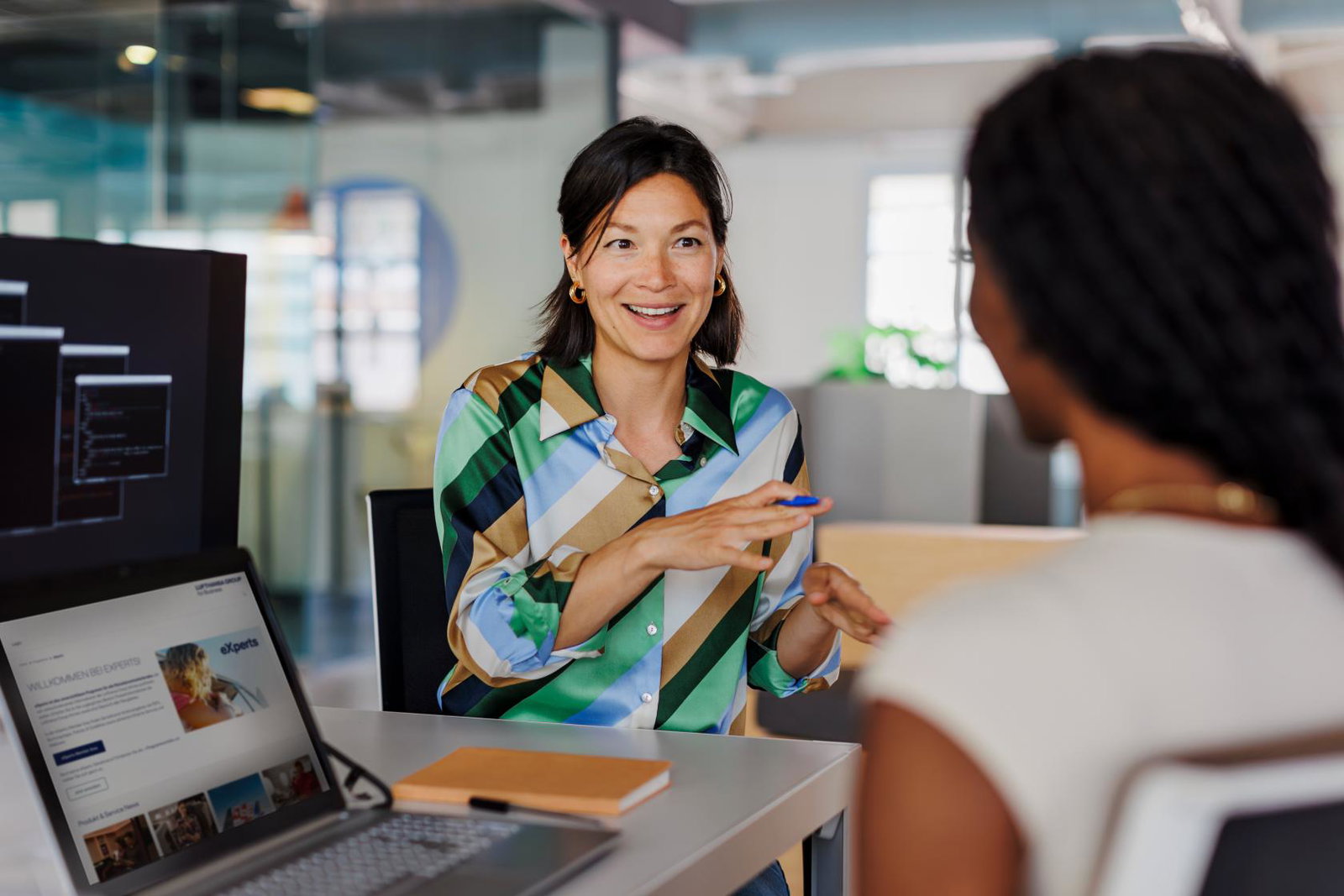 Two women sitting in office environment with laptops open