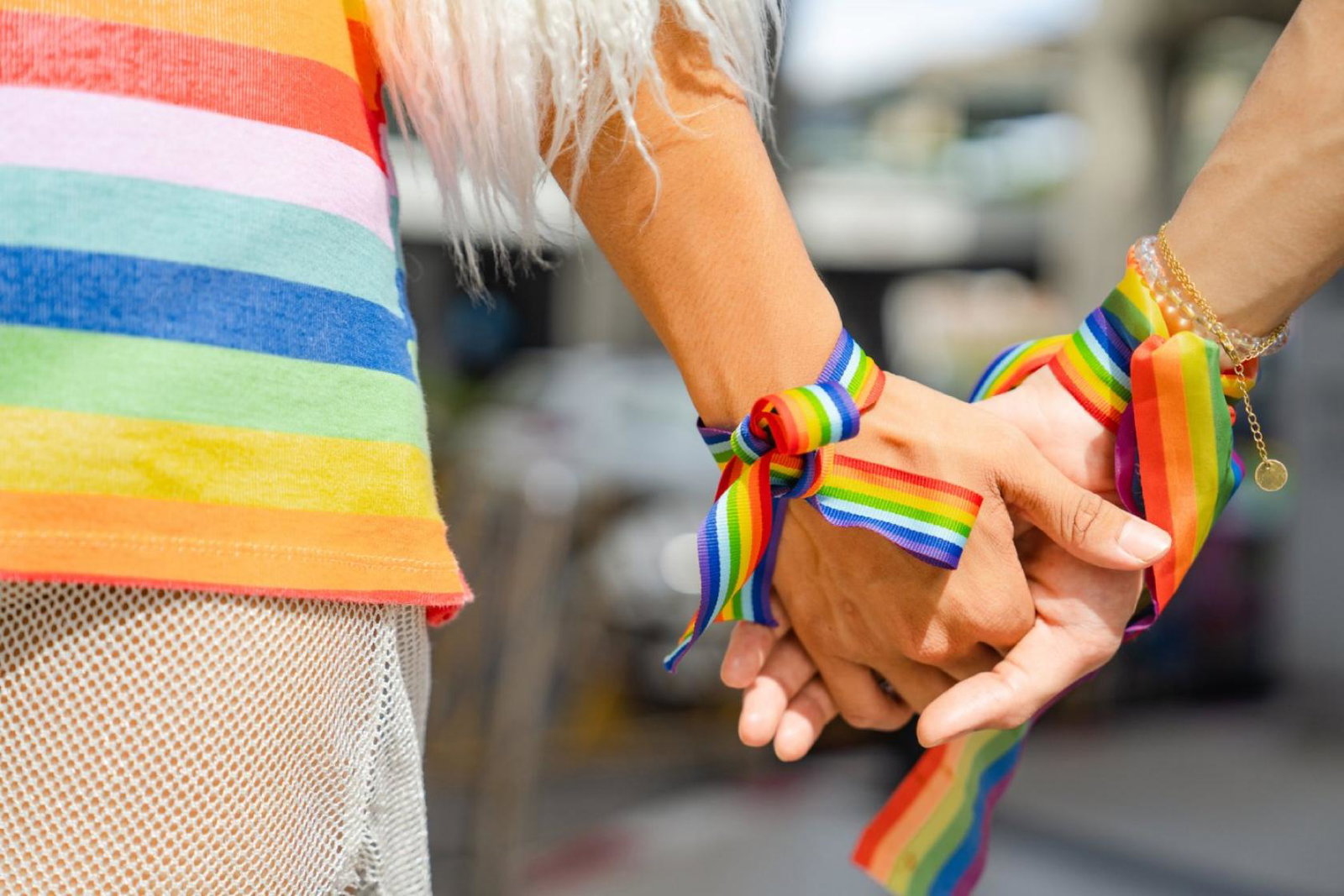 Two people wearing rainbow wristbands clasp hands