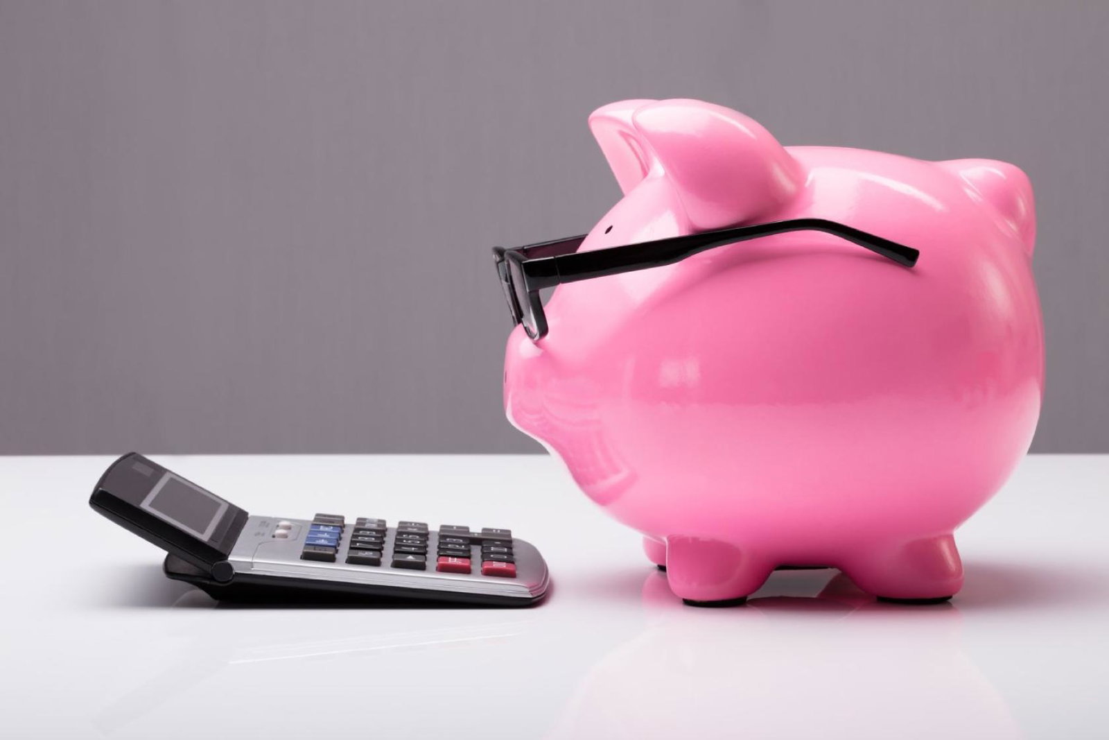 A biggybank pig wearing spectacles looking at a calculator