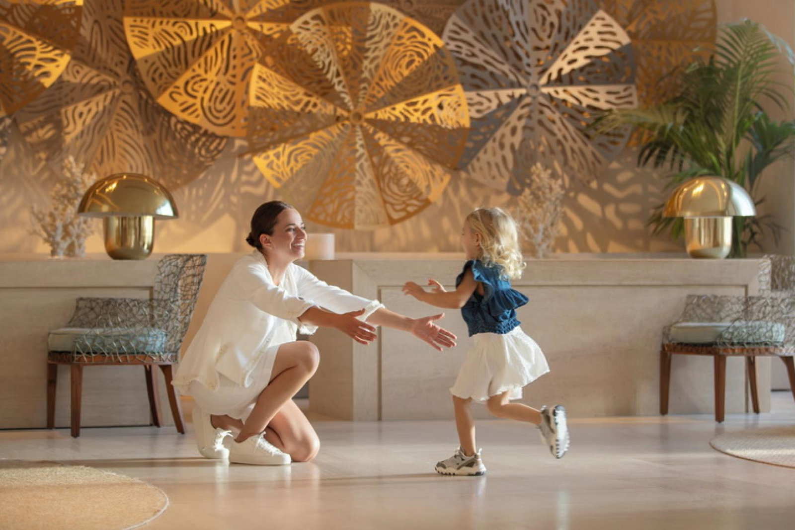 Girl toddler running into the arms of her smiling mum in hotel lobby