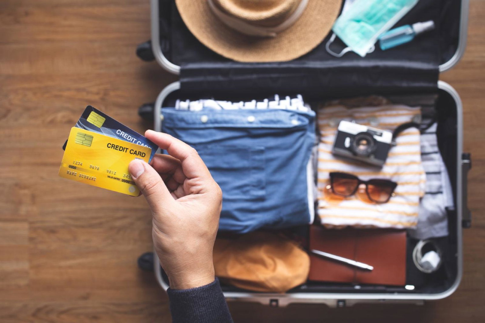 A person holding two bank cards with a half-packed suitcase in the background