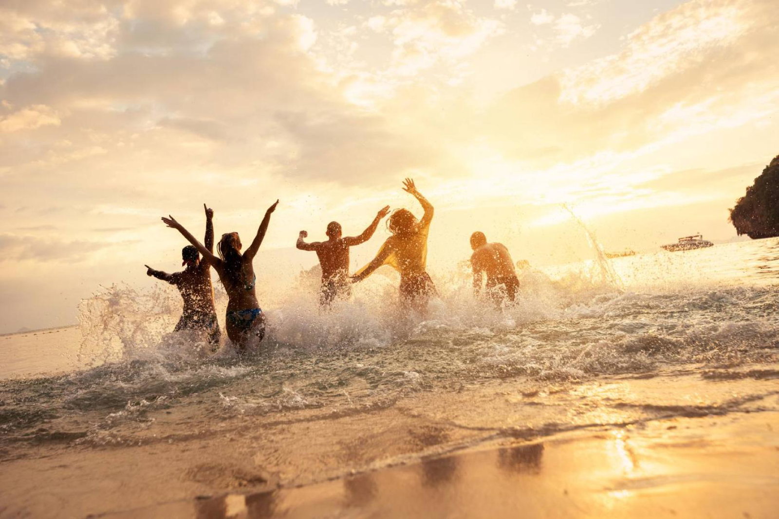 Friends splashing on beach, silhouetted by sunset