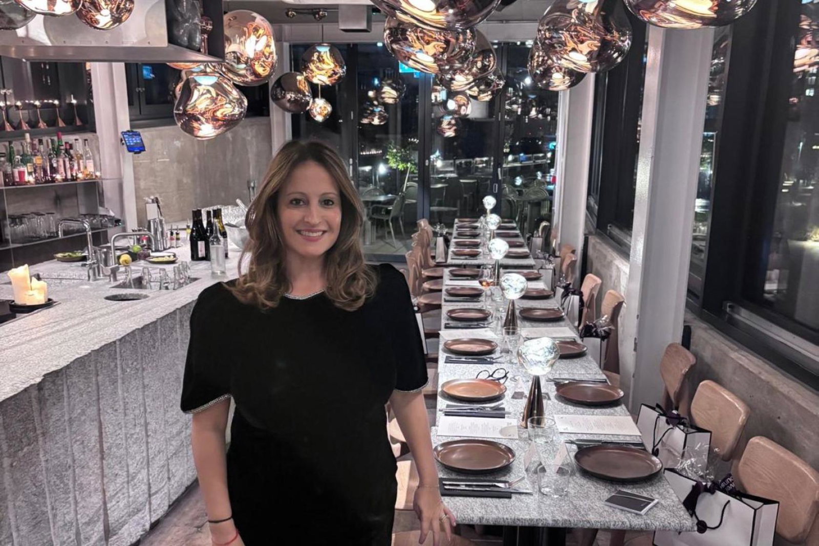 Sara Greene, brown-haired smiling woman standing in front of long dining table 