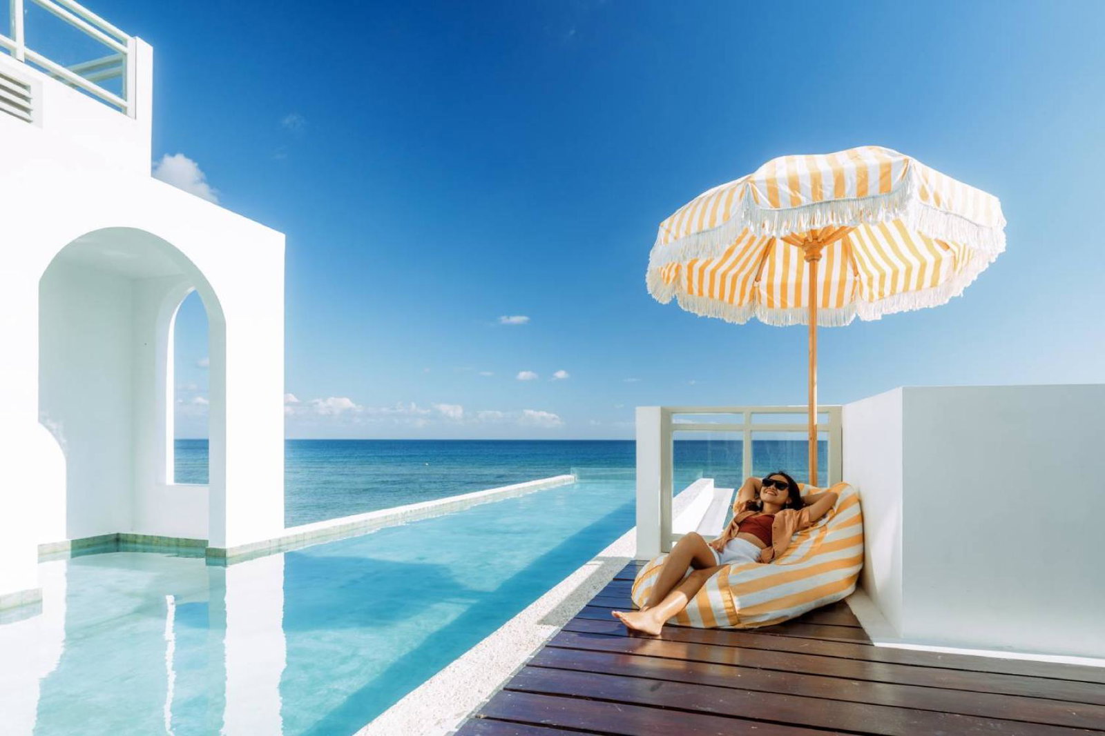 Girl relaxing on sun lounger in beachside resort with infinity pool