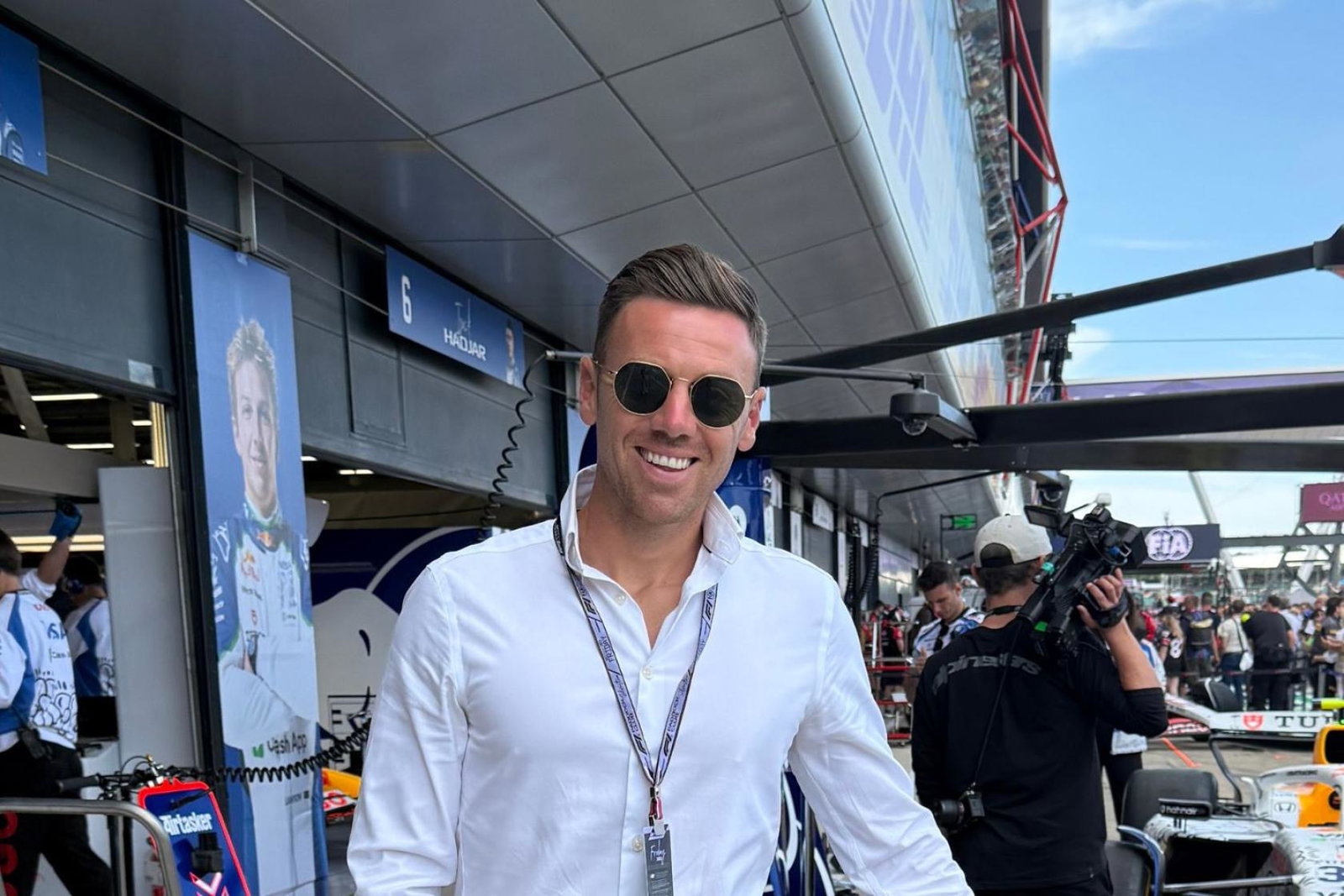 Smiling man wearing sunglasses and white shirt, F1 background 