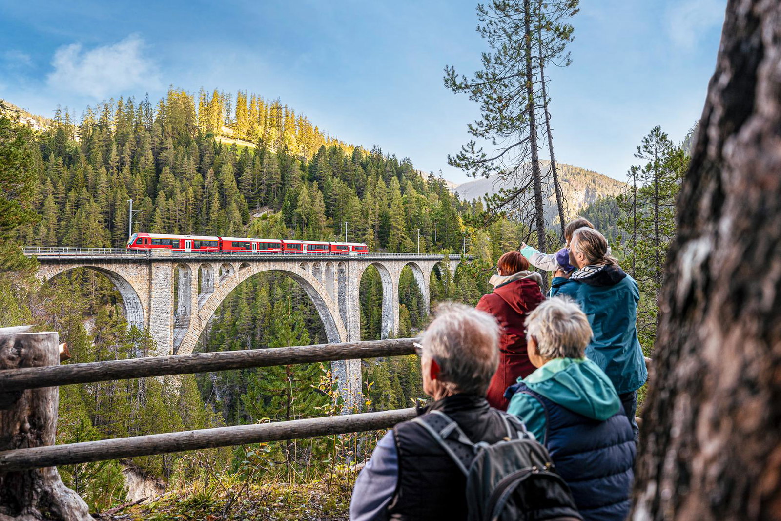 People viewing the Landwasser Viaduct with train going over it from a distance 