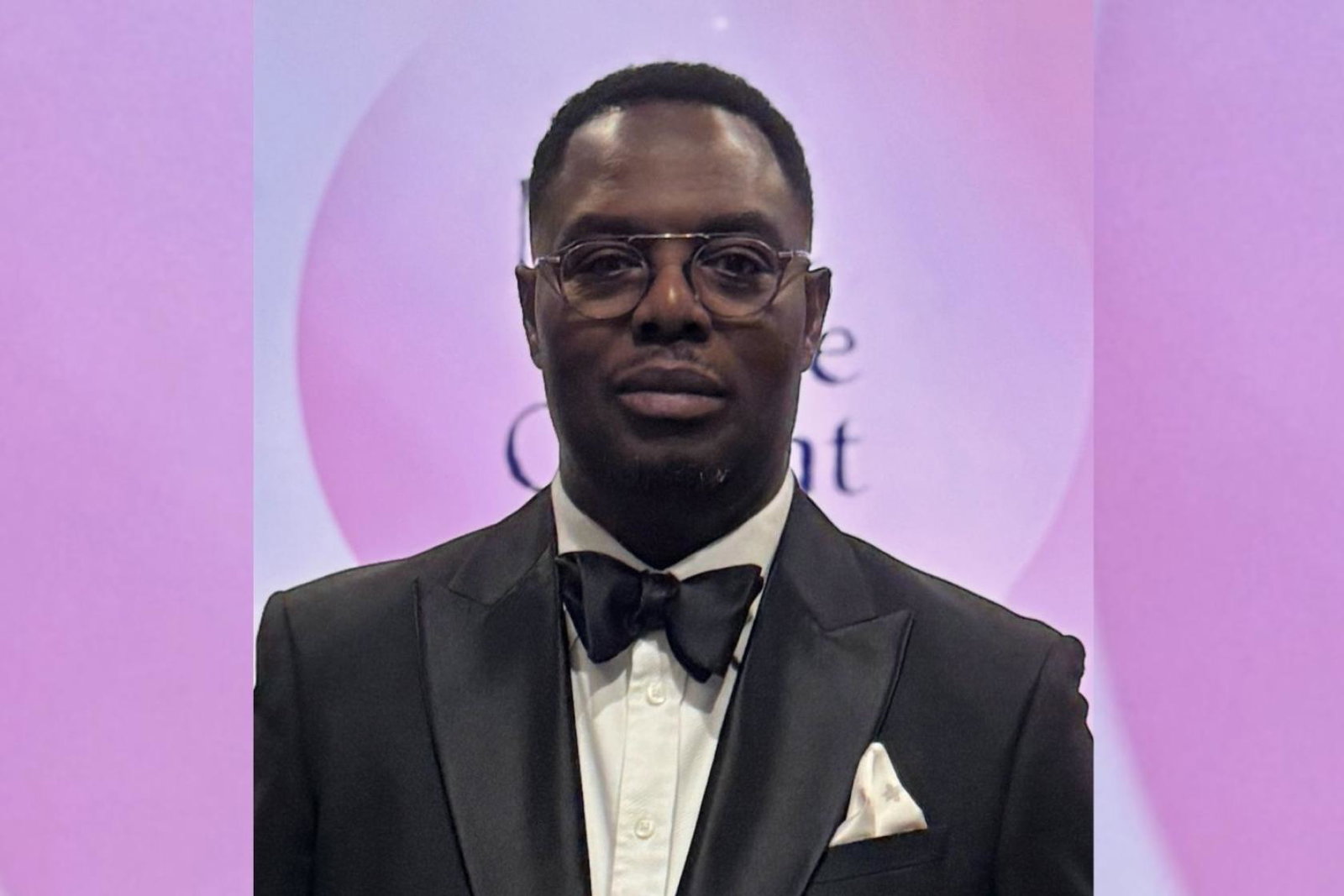 Black man wearing tuxedo, soft pink background 