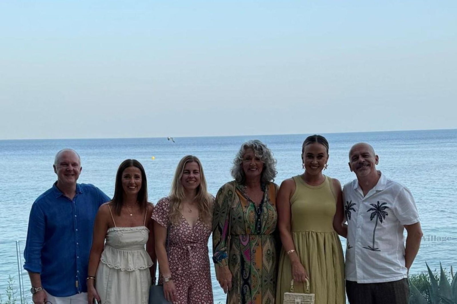 Six people, two men and four women, smiling in front of a beach 