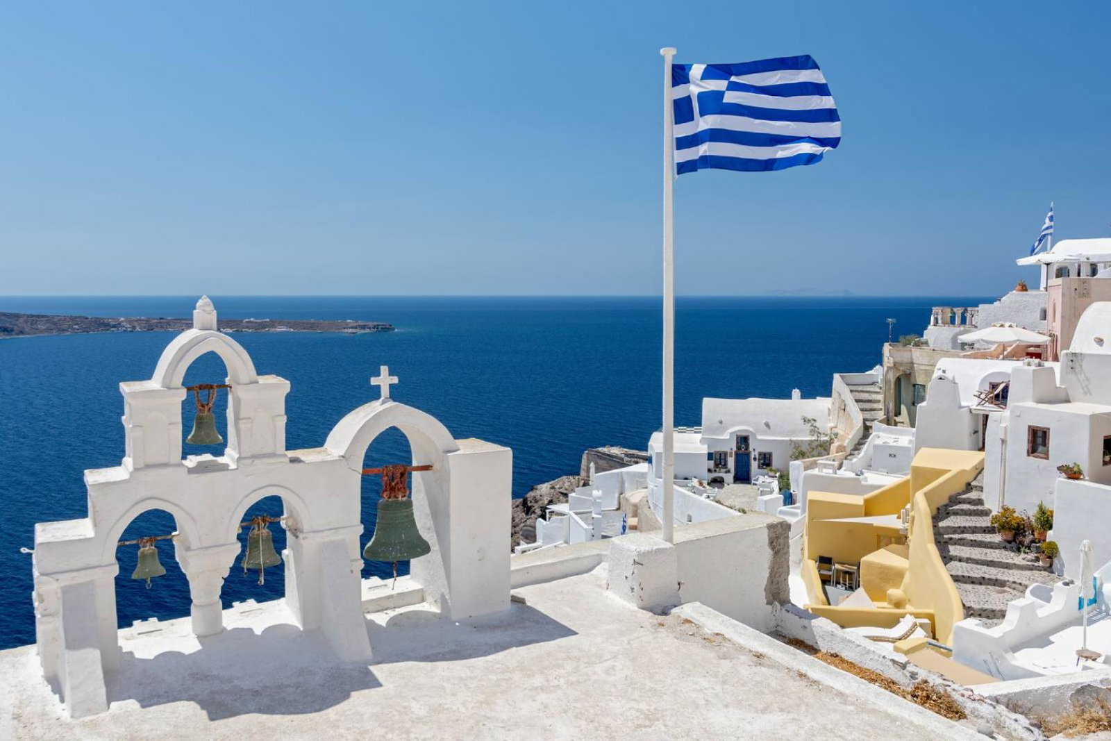 Greek orthodox church with bells and greek flag against famous white houses on Santorini island, Aegean sea, Greece