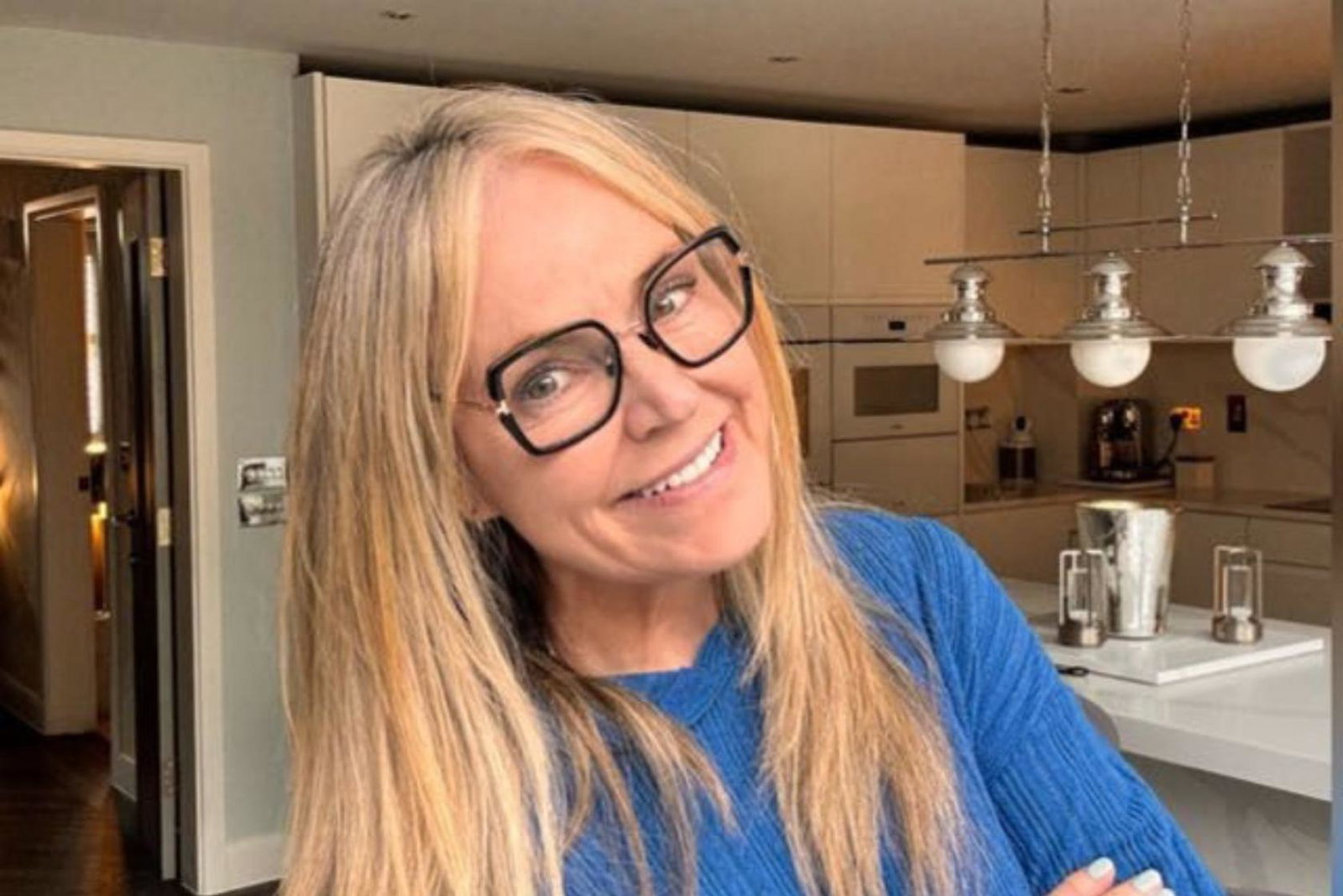 Woman smiling with blonde hair and glasses, her background is a modern kitchen