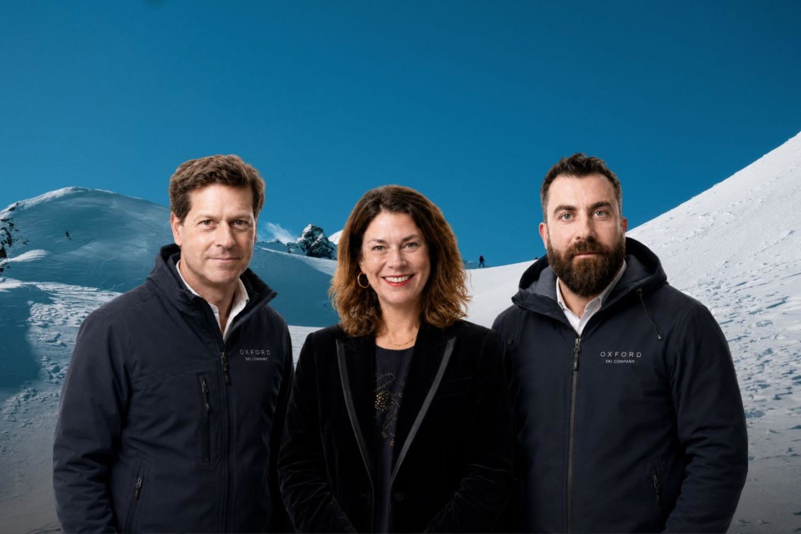 A professional image of a white smiling woman standing with two white men on each side of her, background is snowy ski slopes 