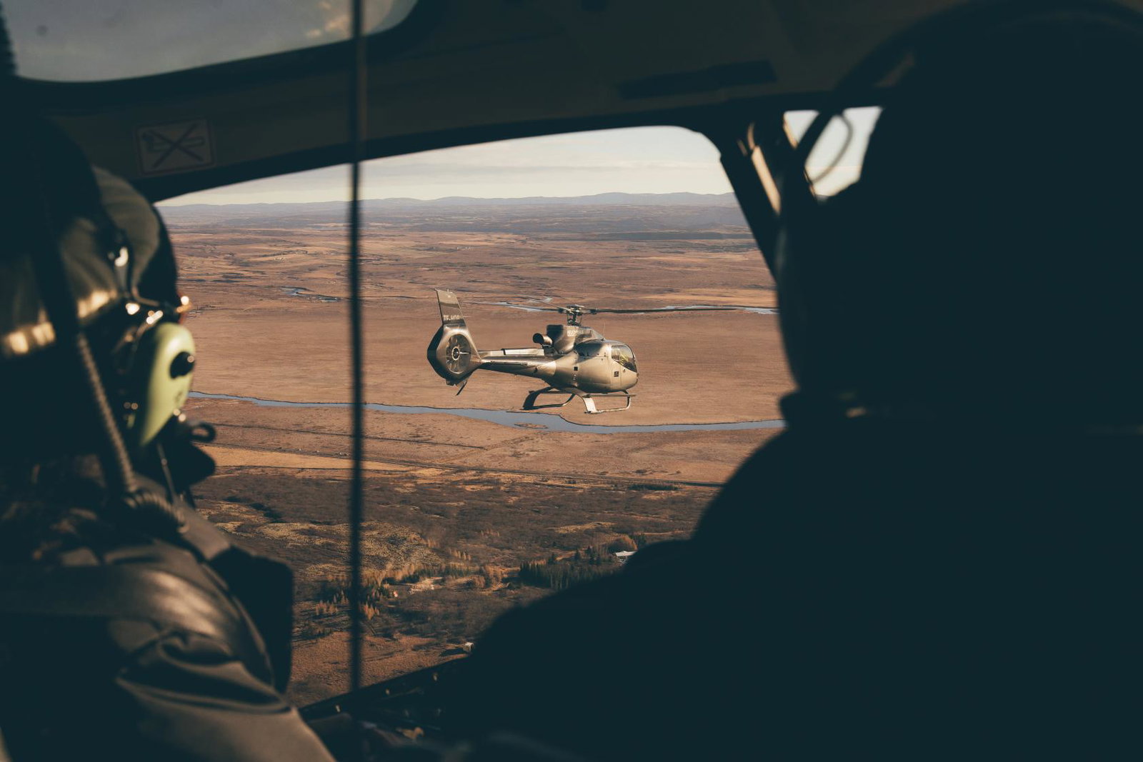 Image shows view out of helicopter to another helicopter flying over Iceland