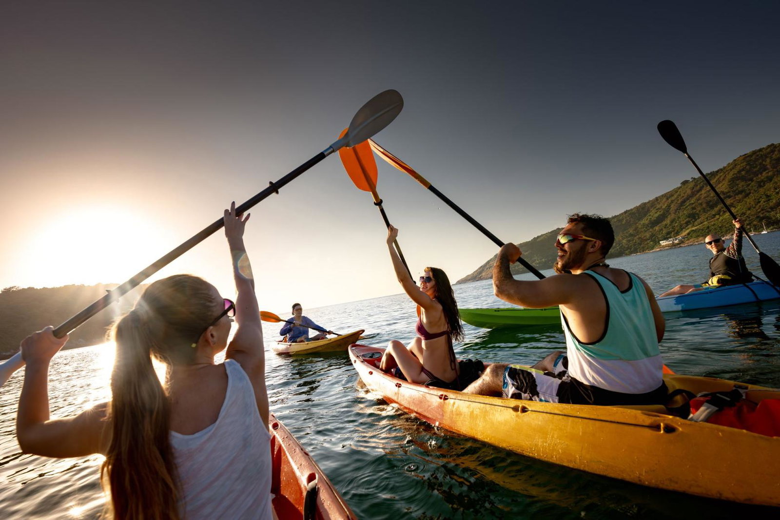 A group out kayaking raise their oars against the sunset