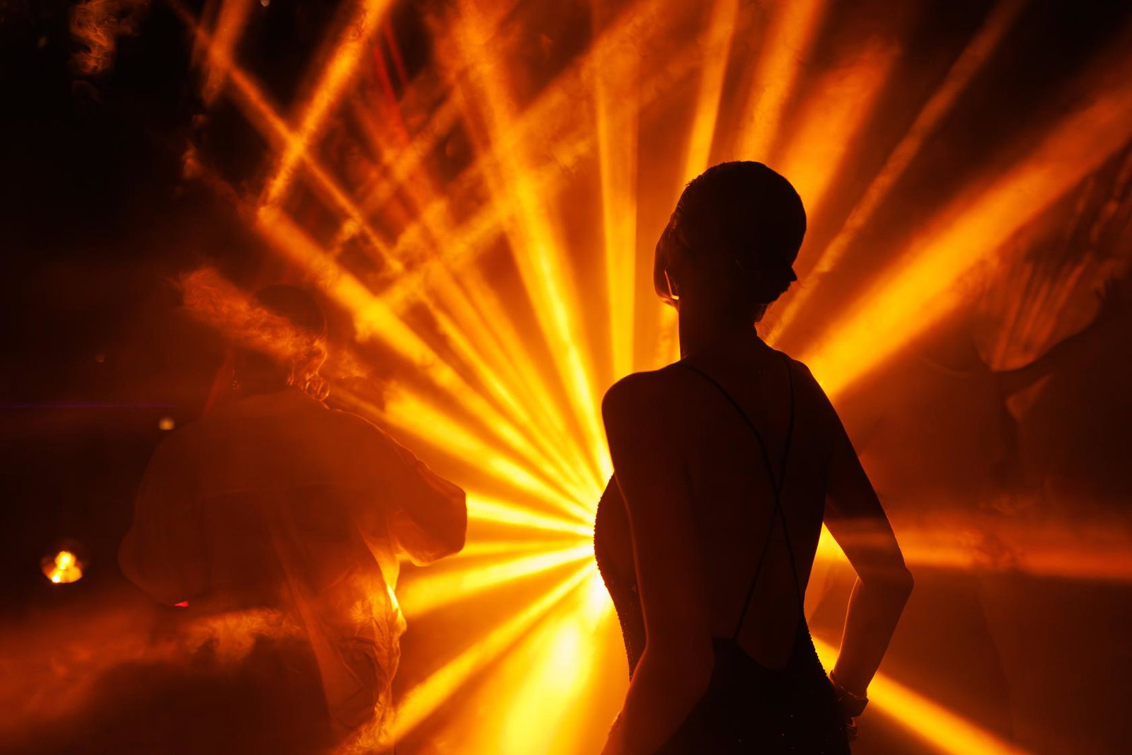 Silhouette of a person dancing in the dark with light beams in the backgroun