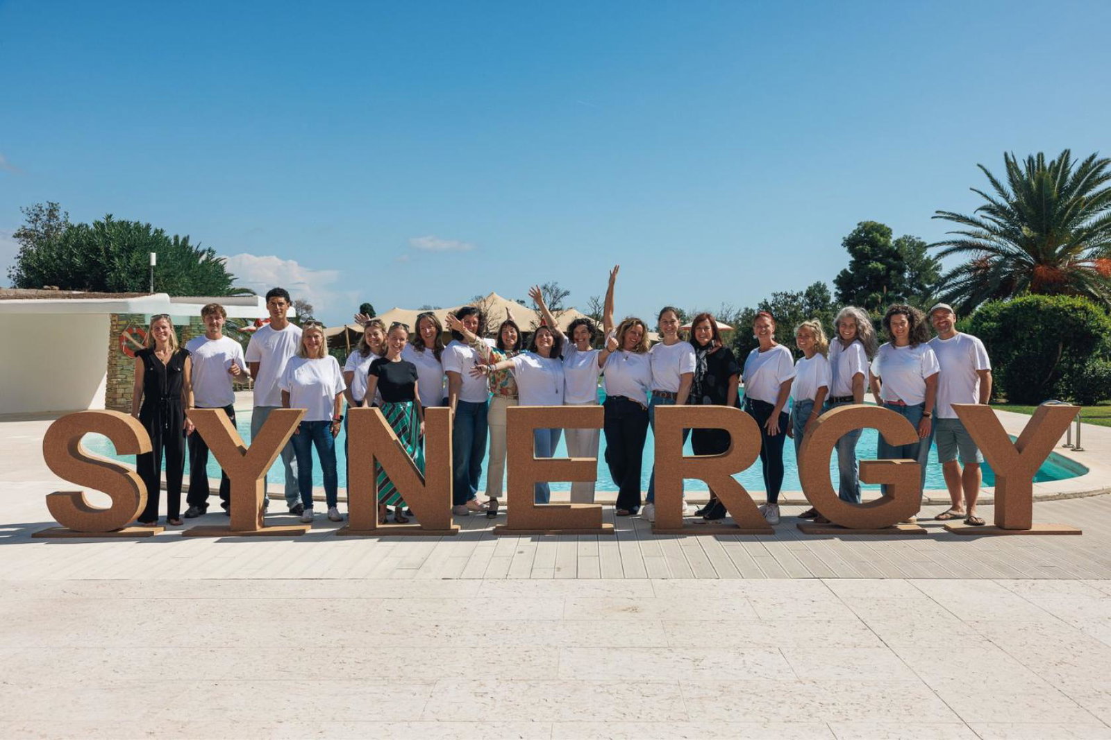 Group of people in front of a large sign that says 'Synergy' 