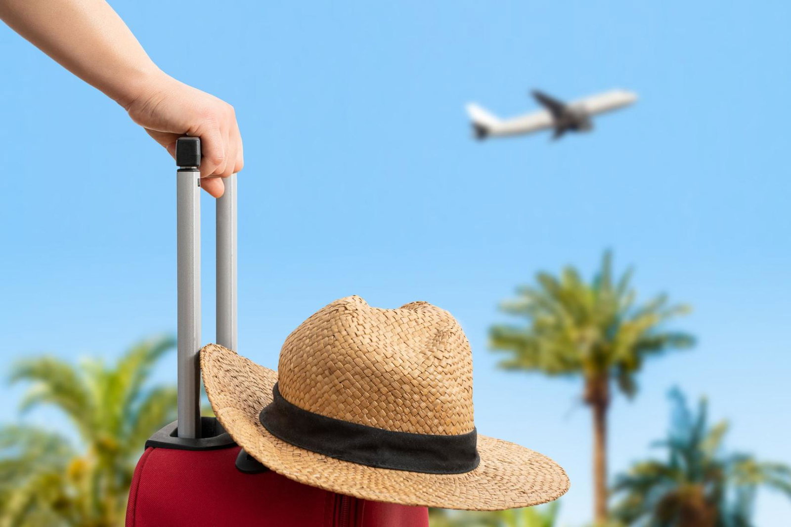 A passenger waits with a suitcase and hat as an aircraft takes off