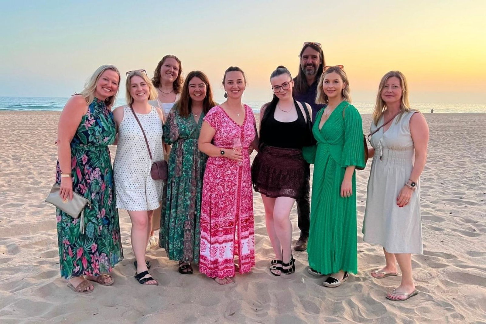 People standing on a white sand beach with the sunset behind them