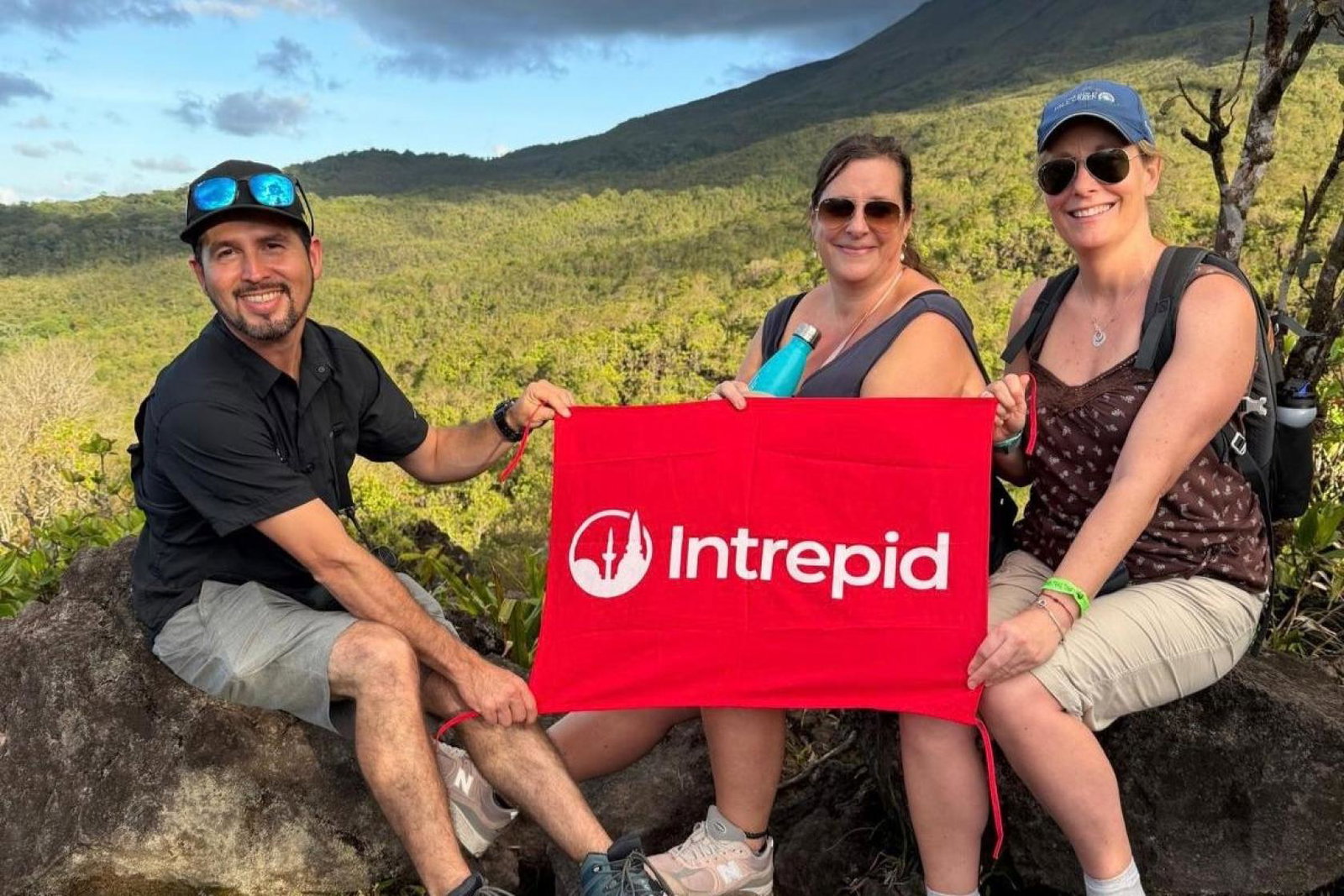 Claire Spicer and two other people holding Intrepid sign up with green jungle in background