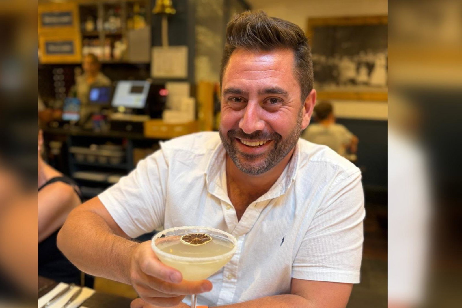 White man with brown short hair smiling and holding cocktail 