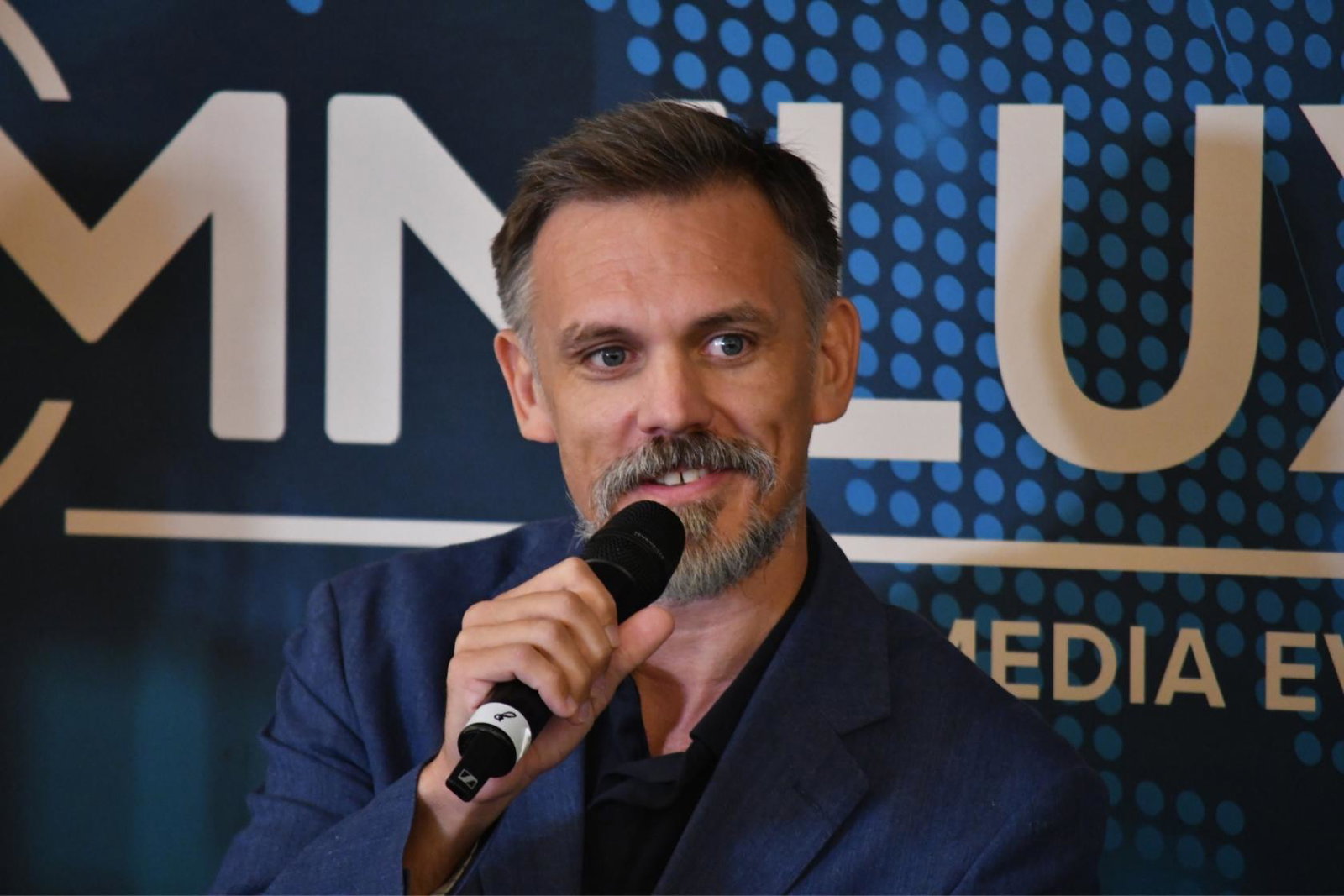 White man speaking on stage with microphone