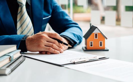 A person sorting their tax affairs at a desk with files, pen and a small model house