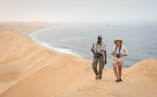 People walking over giant sand dunes with ocean behind