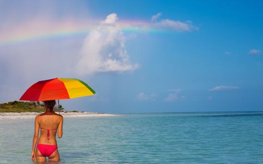 A woman pictured in the sea with an umbrella beneath a rainbow