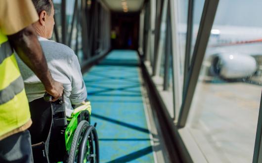 A air traveller being pushed down an air bridge onto an aircraft in a wheelchair