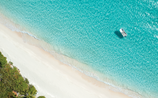 Drone photo of blue ocean water, white sand beach and trees