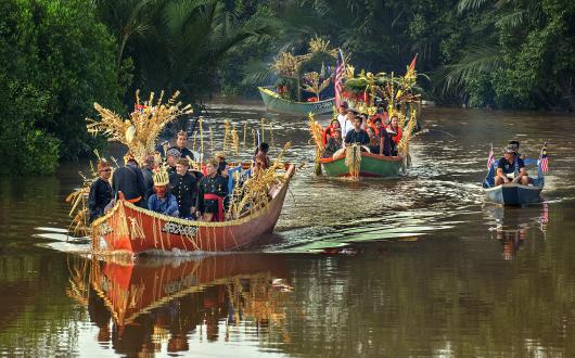 Sarawak locals in two boats moving down a brown river for a festival