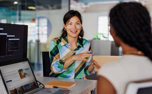 Two women sitting in office environment with laptops open