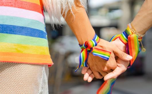 Two people wearing rainbow wristbands clasp hands