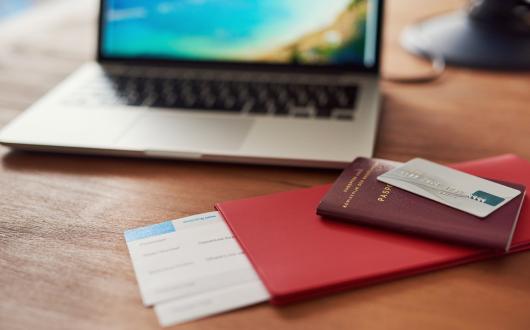 A passport, boarding card and bank card pictured with a laptop in the background