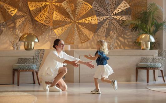 Girl toddler running into the arms of her smiling mum in hotel lobby