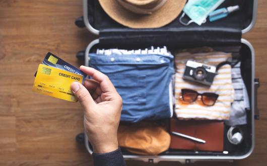 A person holding two bank cards with a half-packed suitcase in the background