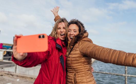 Two women take a selfie with the sea in the background