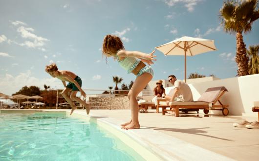 Two children mid-air jumping into a swimming pool 