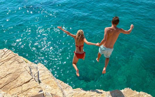 Couple jumping from small cliff into sea