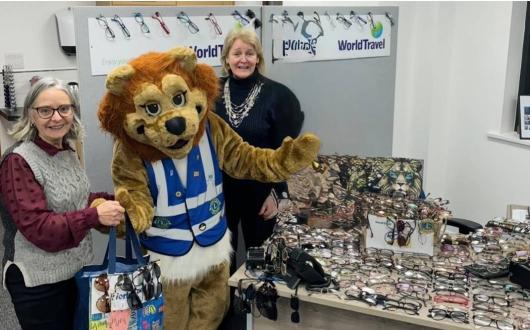 Team at Travel World Jersey next to Lions Club of Jersey mascot and collected glasses