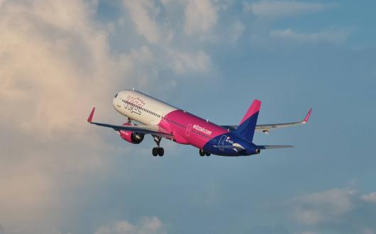 Wizz Air plane mid-flight against a slightly cloudy backdrop