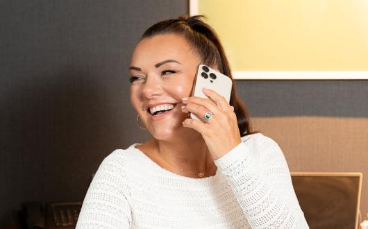 Brown haired woman smiling, she is on the phone 