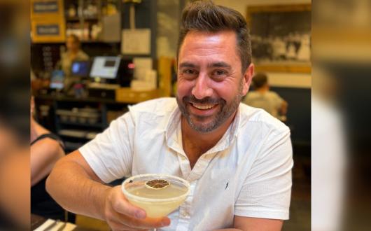 White man with brown short hair smiling and holding cocktail 