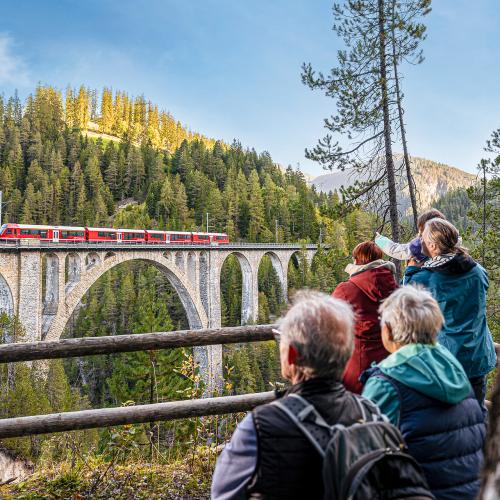 People viewing the Landwasser Viaduct with train going over it from a distance 