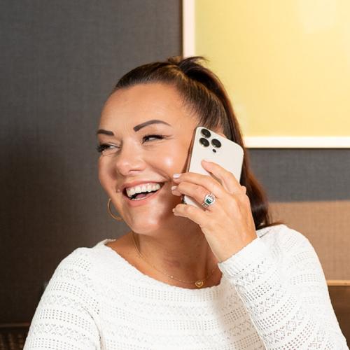 White woman with brown hair in ponytail, smiling and talking on the phone 