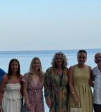 Six people, two men and four women, smiling in front of a beach 
