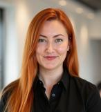 White woman with long, straight red hair and black shirt smiling at camera