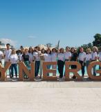 Group of people in front of a large sign that says 'Synergy' 