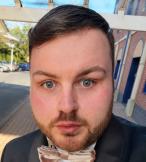 Professional headshot of young white man with short brown hair and tuxedo  